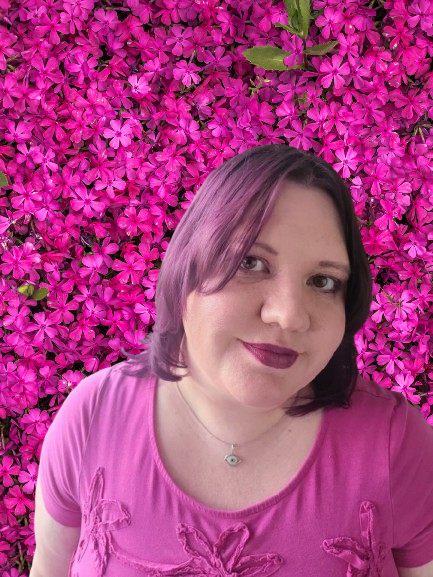 Artist Lindsey McConnell smiling in front of a dense backdrop of vibrant magenta blossoms