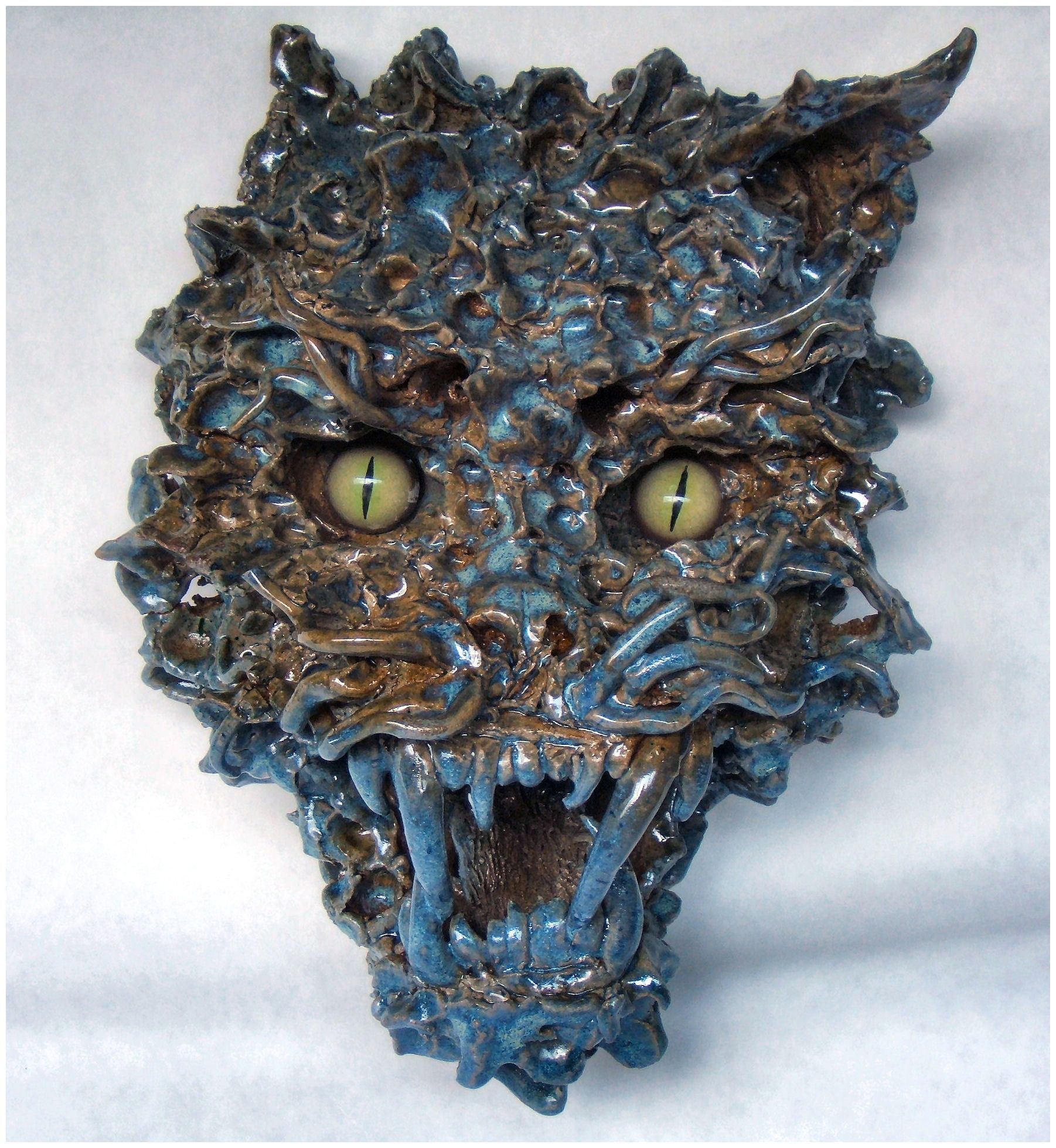 Textured ceramic wall sculpture of a snarling wildcat with mottled cobalt glaze, open jaws showing fangs, and cat-slit green eyes